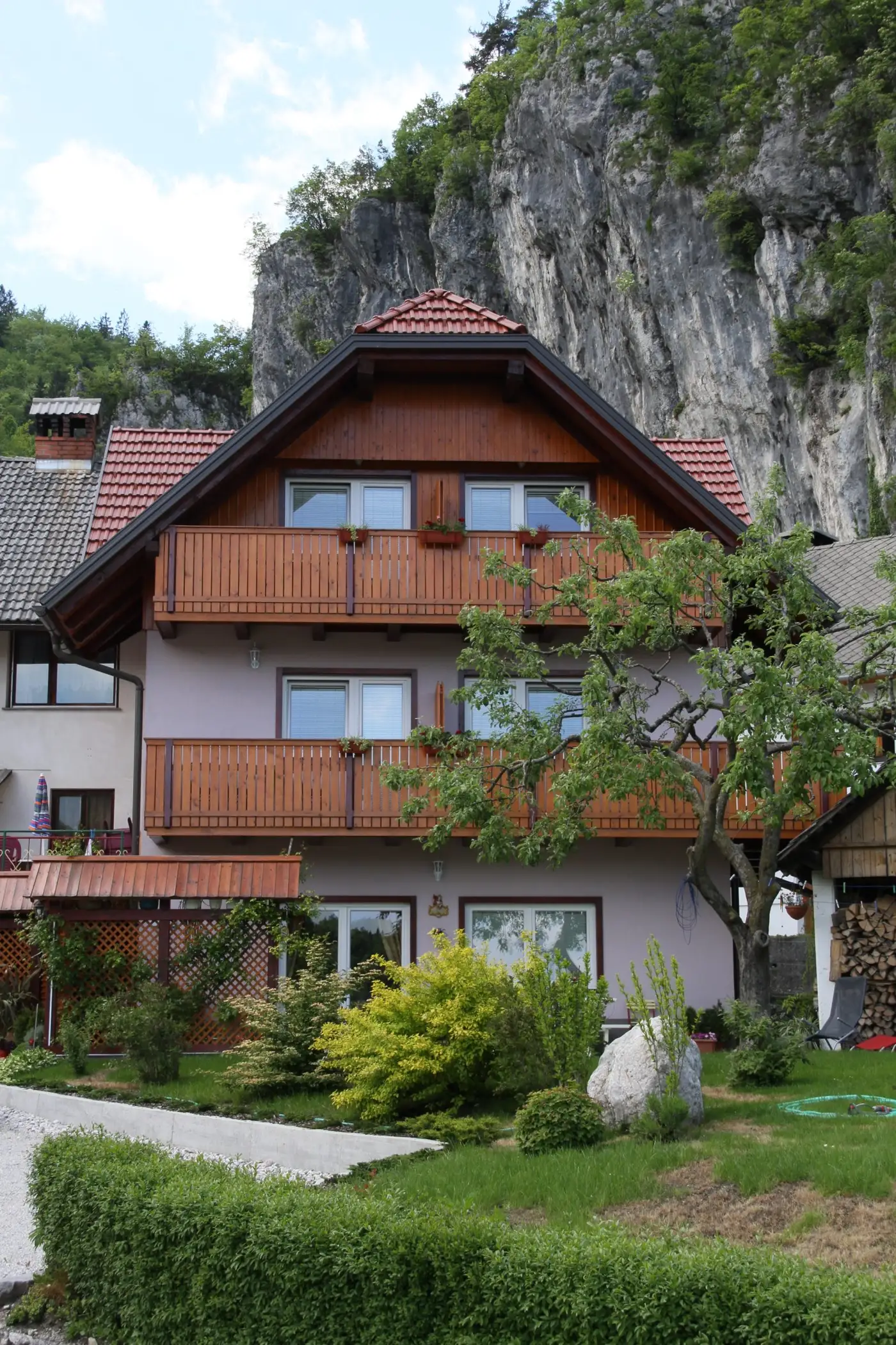 Naša hiša z lesenimi balkoni, za njo skalne pečine